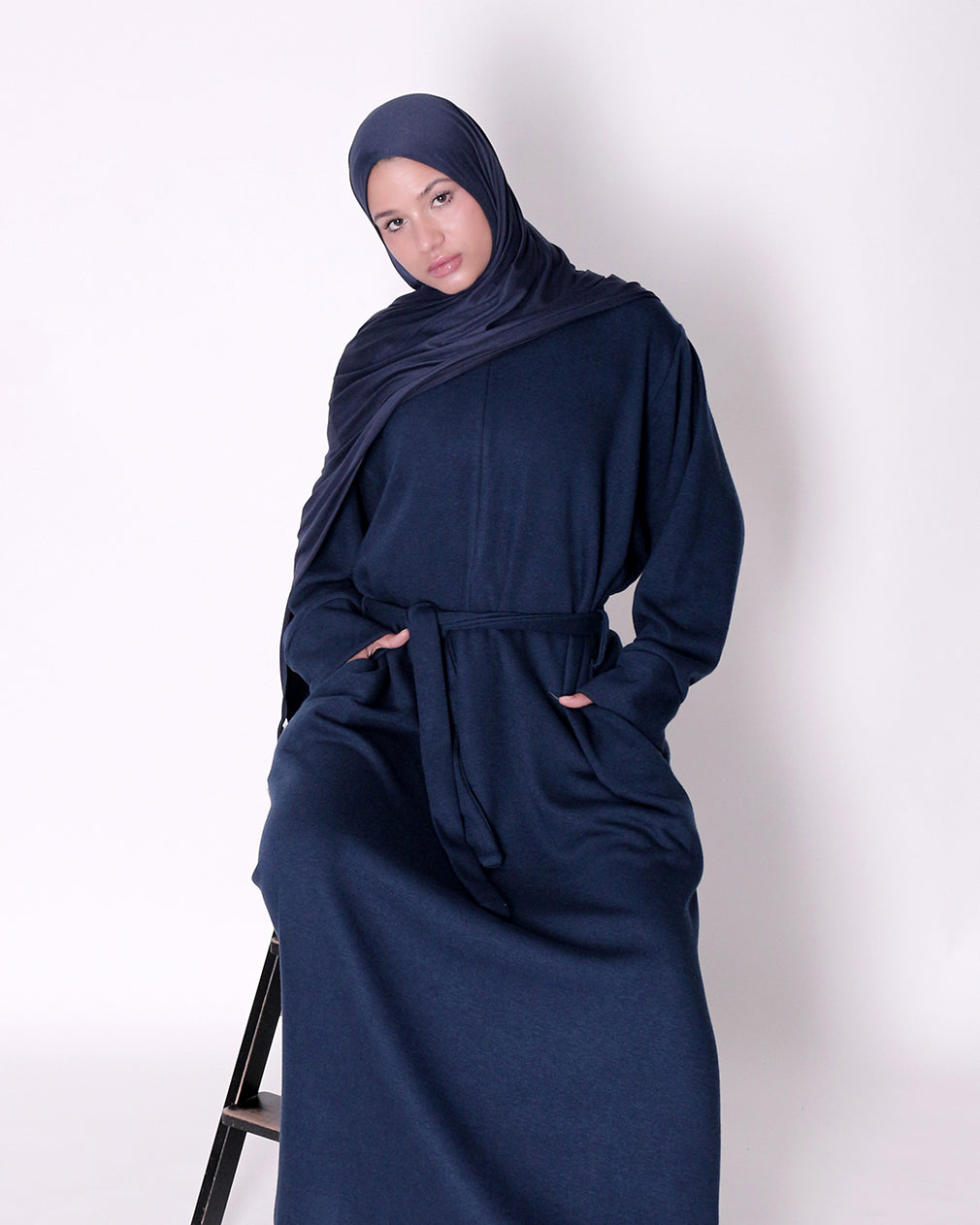 Woman wearing a navy blue abaya and hijab on a white background