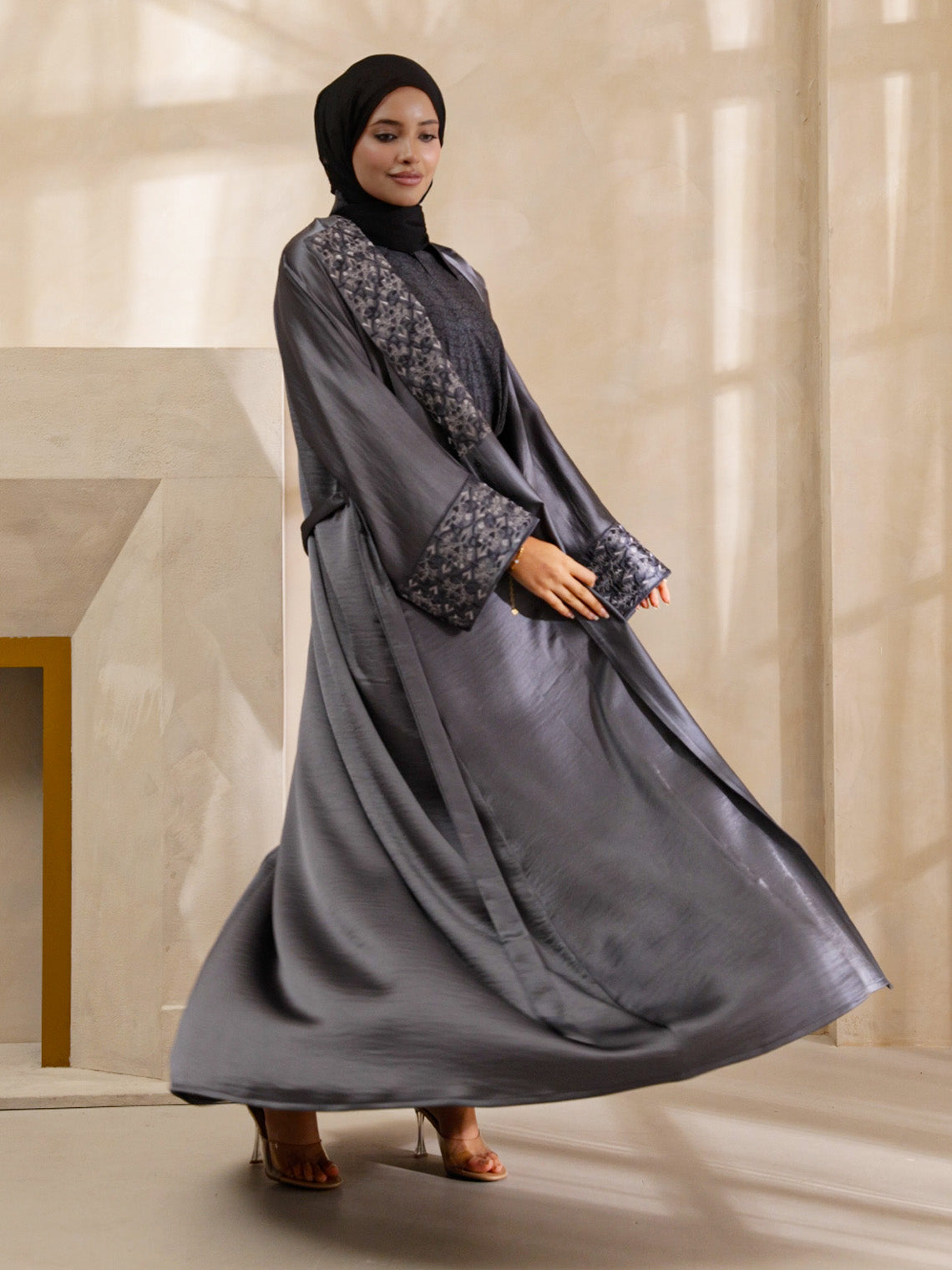 Woman wearing a gray abaya with floral patterns in a neutral setting
