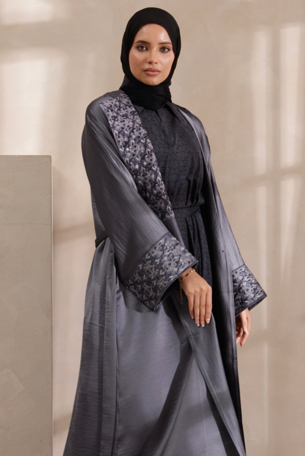 Woman wearing a gray abaya with floral patterns on a neutral background