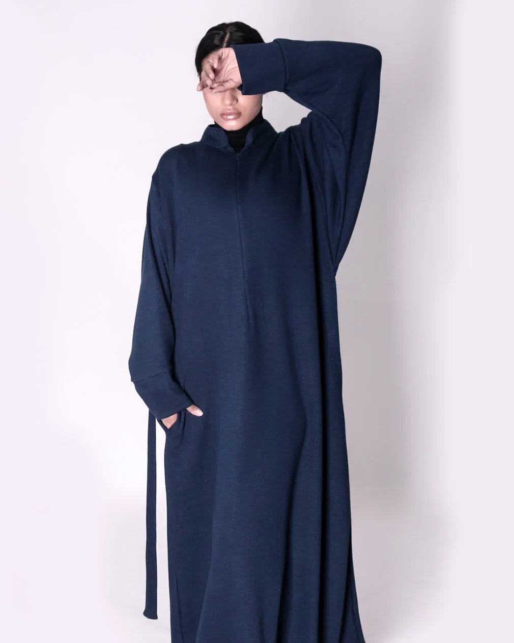 Person wearing a long navy blue abaya dress with a high collar on a white background