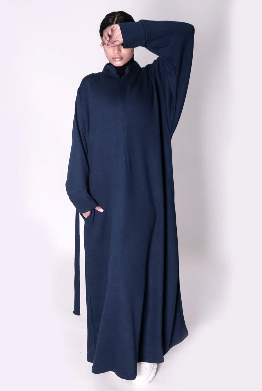 Person wearing a long navy blue abaya dress with a high collar on a white background