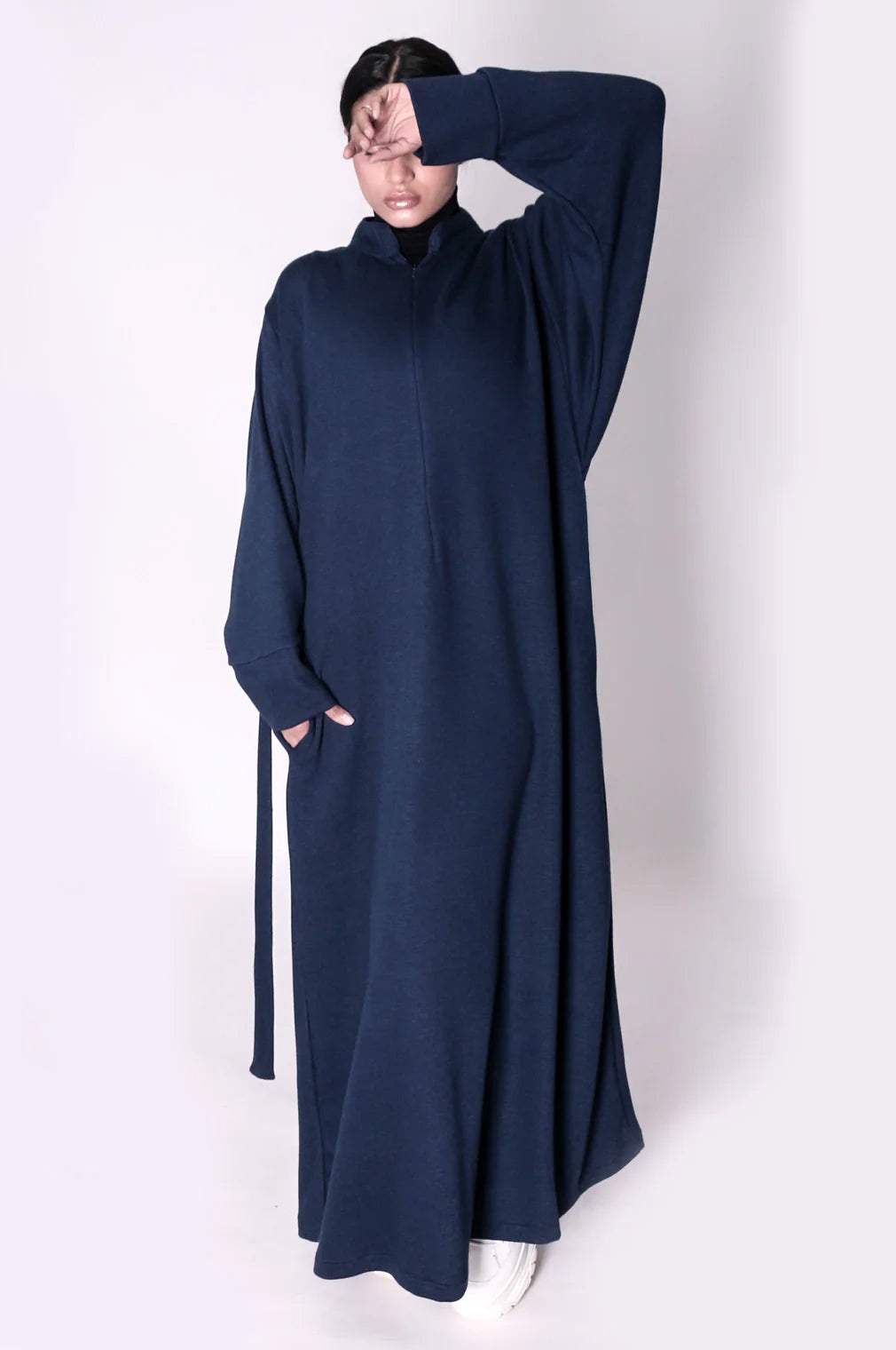 Person wearing a long navy blue abaya dress with a high collar on a white background