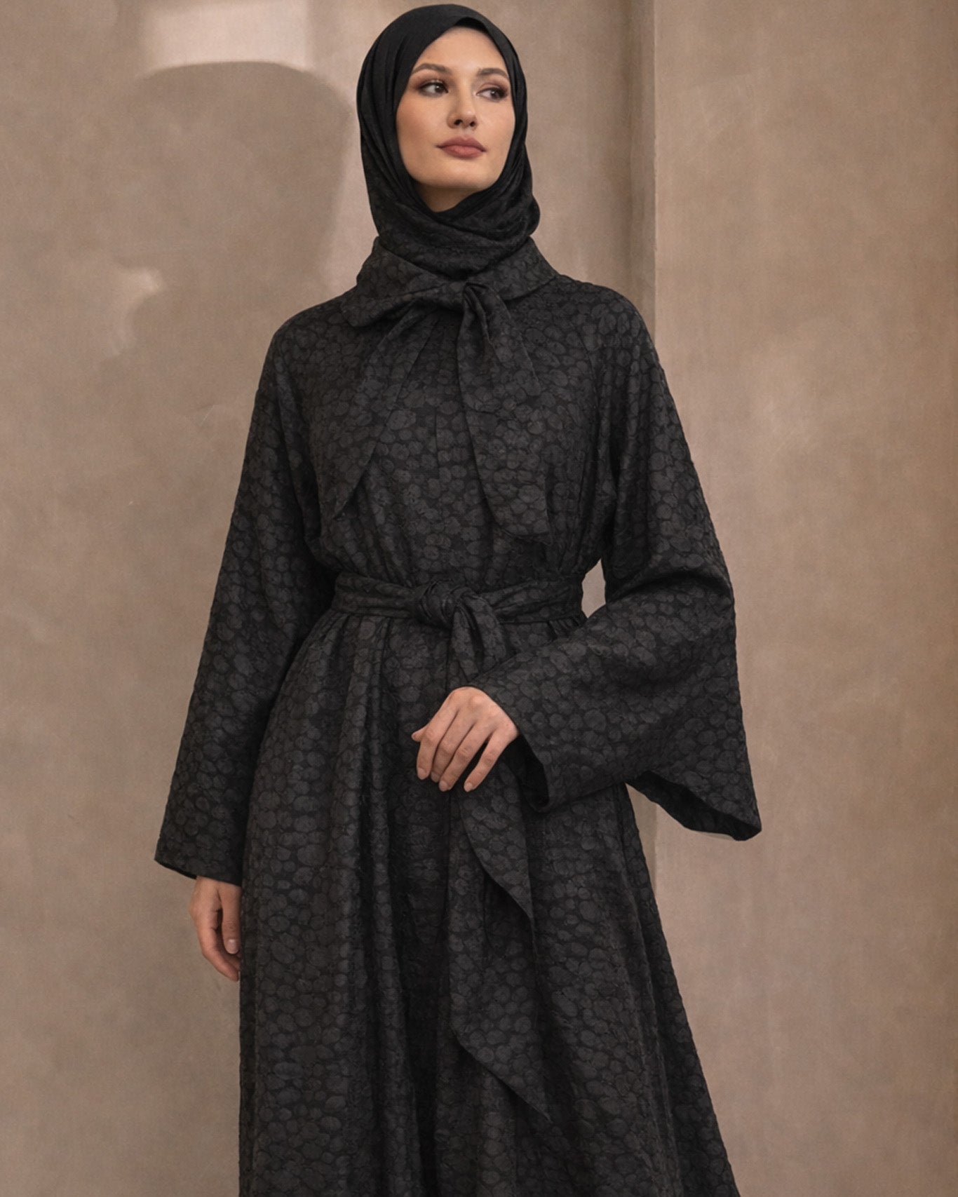 Woman wearing a black patterned dress against a beige background