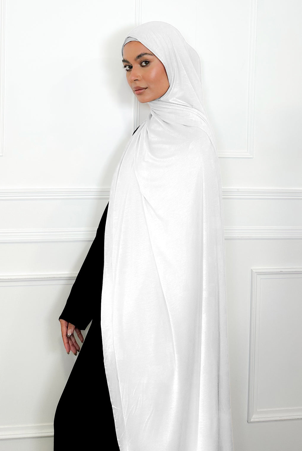 Woman wearing a white hijab and black outfit against a white wall ideal for umrah