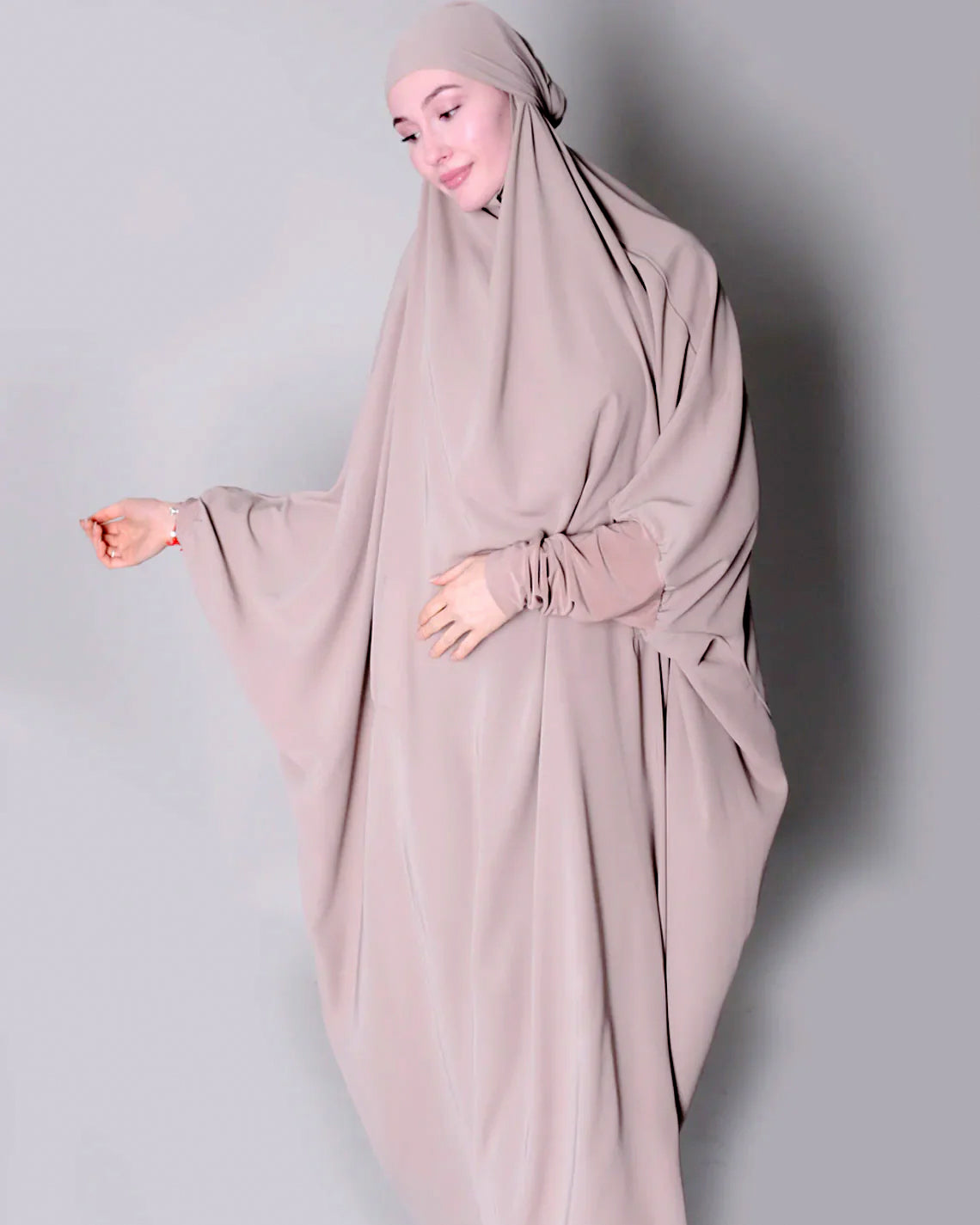 Person wearing a beige hijab and dress against a plain background one piece jilbab abaya