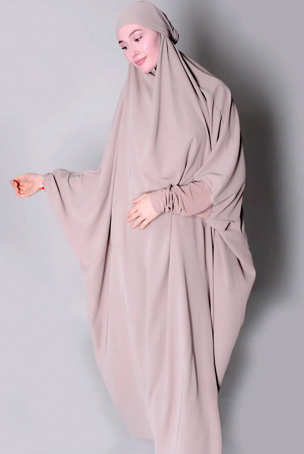 Person wearing a beige hijab and dress against a plain background one piece jilbab abaya