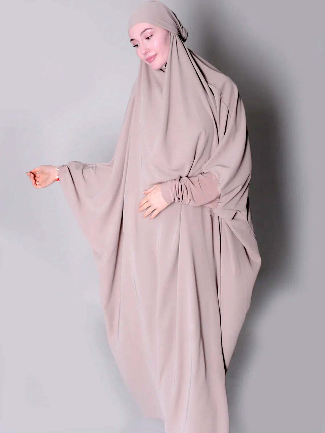 Person wearing a beige hijab and dress against a plain background one piece jilbab abaya