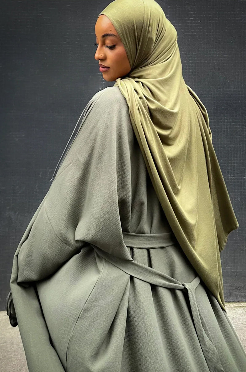 Woman wearing a green hijab and matching outfit against a dark background, khaki kaftan