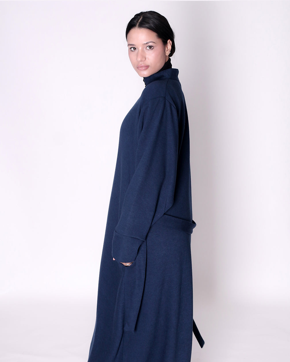 Woman wearing a long navy blue dress abaya against a white background