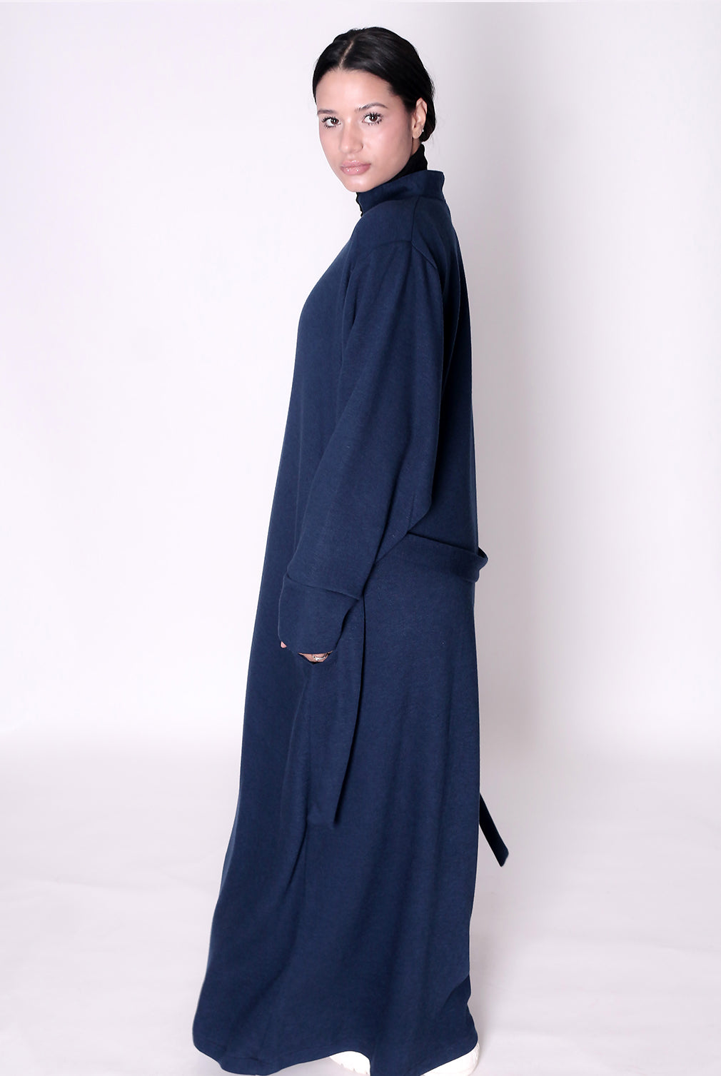 Woman wearing a long navy blue dress abaya against a white background