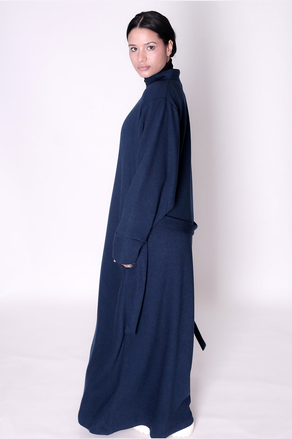 Woman wearing a long navy blue dress abaya against a white background