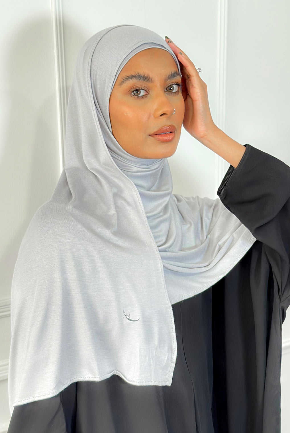 A woman wearing a light grey modal jersey hijab with a plain background.