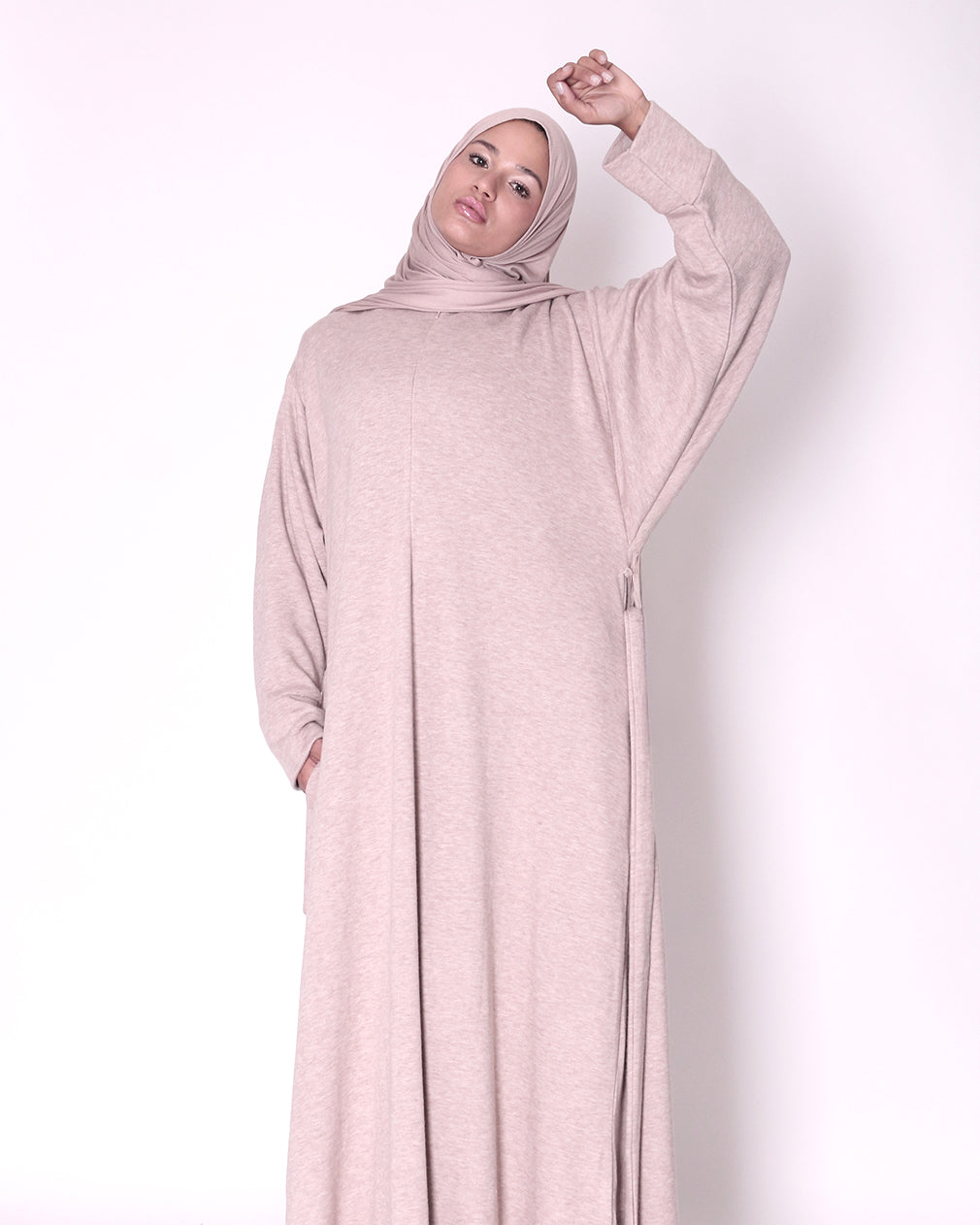 Woman wearing a long, light pink dress knitted abayawith a hood on a white background