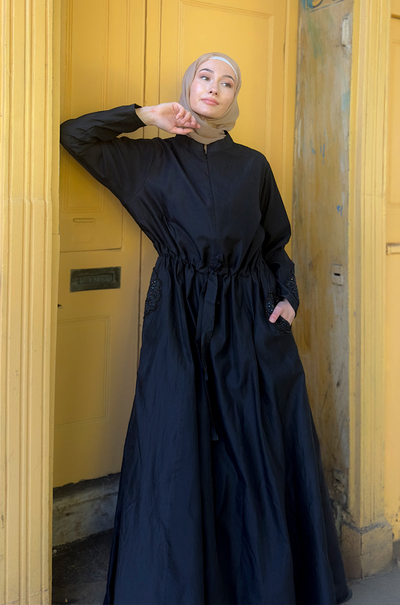 Woman in a long black dress standing in a doorway with yellow walls.