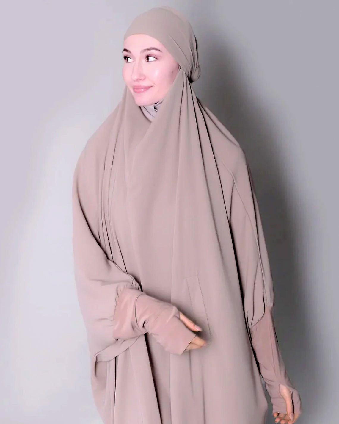 Woman wearing a beige hijab and dress against a plain background. one piece jilbab abaya