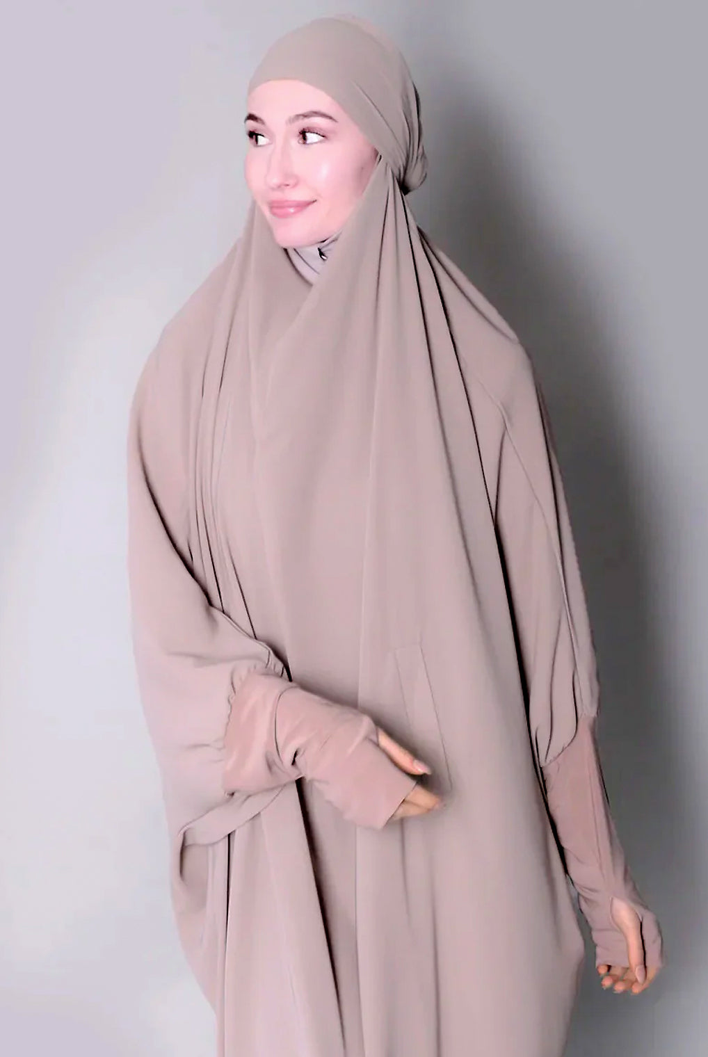 Woman wearing a beige hijab and dress against a plain background. one piece jilbab abaya