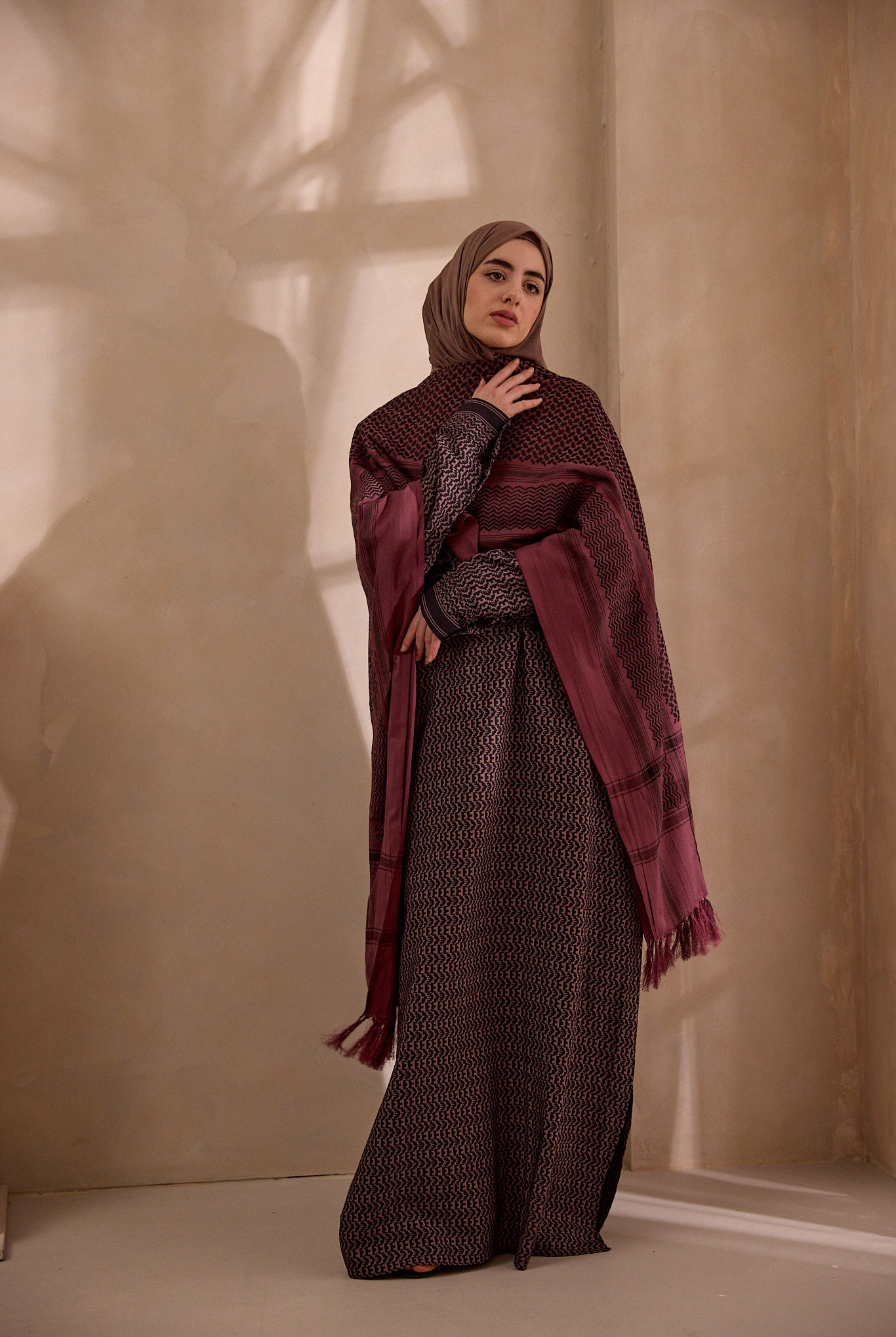 Woman wearing a patterned outfit with a maroon scarf against a beige wall.
