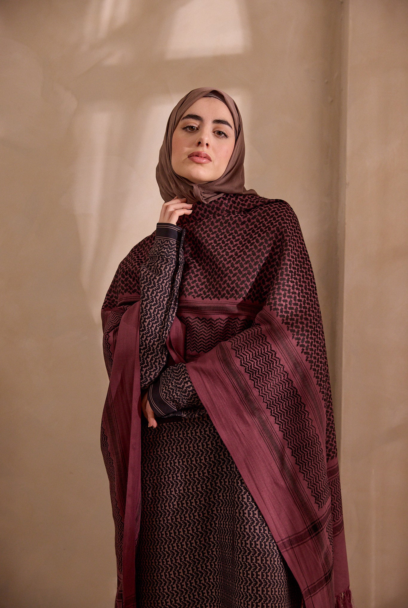 Woman wearing a patterned burgundy hijab against a beige background