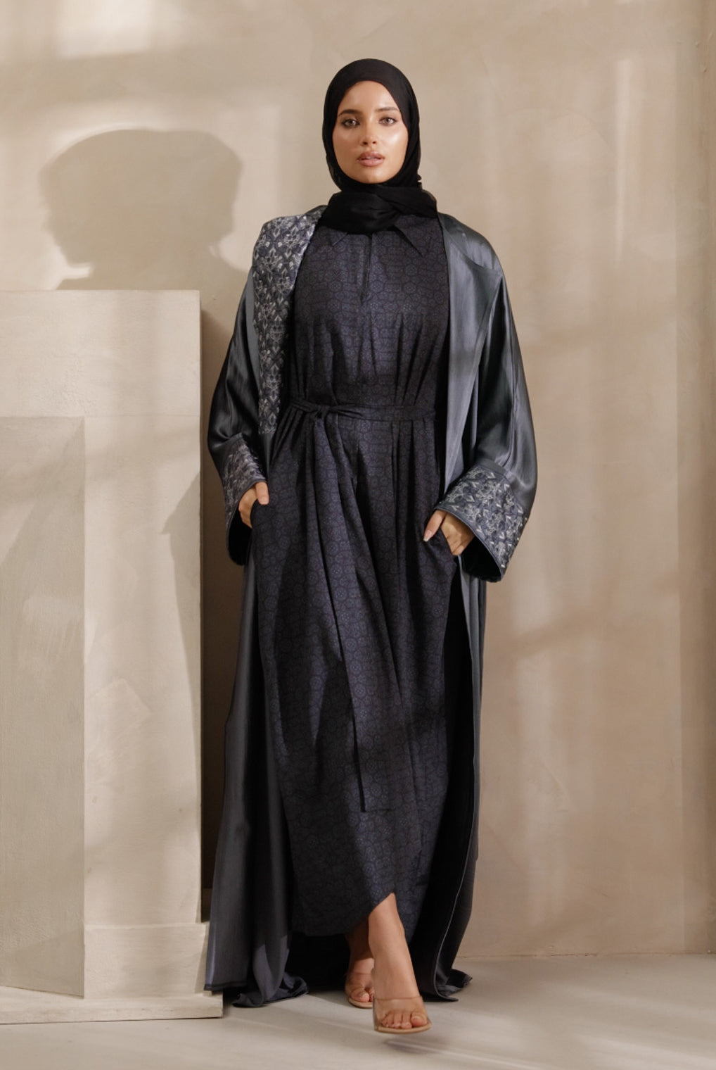 Woman wearing a dark gray abaya with a patterned shawl in a neutral setting