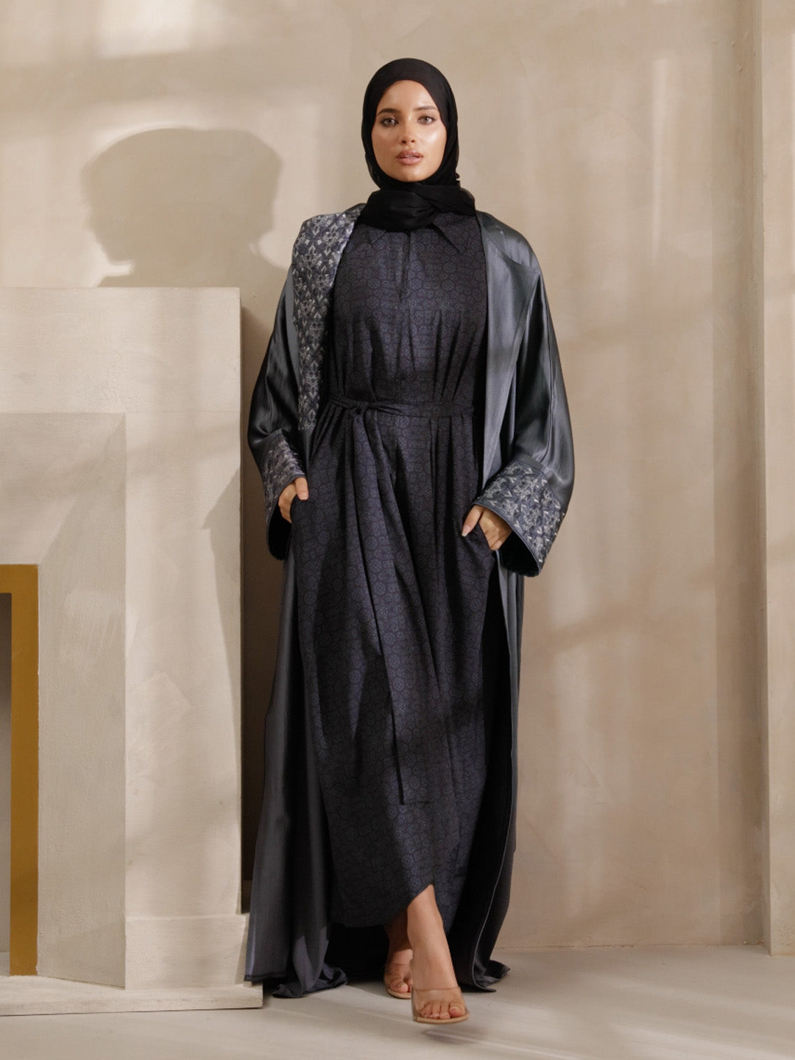 Woman wearing a dark gray abaya with a patterned shawl in a neutral setting