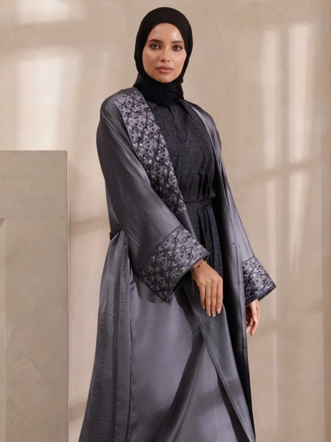 Woman wearing a gray abaya with floral patterns on a neutral background