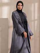 Woman wearing a gray abaya with floral patterns on a neutral background