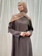 Image depicting a woman wearing a luxurious Hareer Abaya in a neutral brown tone, perfectly complemented by the matching Hareer Jacket. The smooth texture of the silk fabric enhances the graceful drape of the garment, ideal for Spring/Summer fashion.