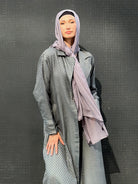 Person wearing a long, light gray khafiyah textured jacket with a matching maxi jersey hijabagainst a dark background