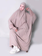 Person wearing a long, light-colored abaya with a matching hijab on a white background. one piece jilbab abaya