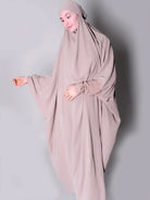 Person wearing a beige hijab and dress against a plain background one piece jilbab abaya