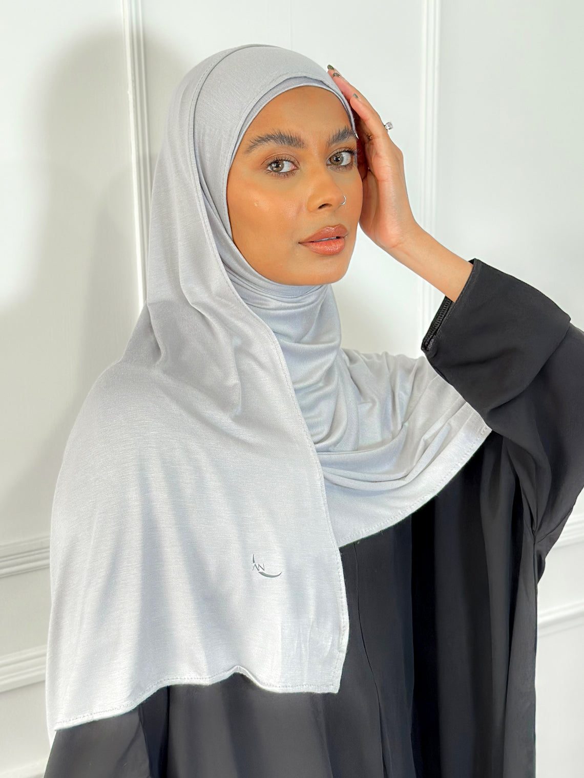A woman wearing a light grey modal jersey hijab with a plain background.