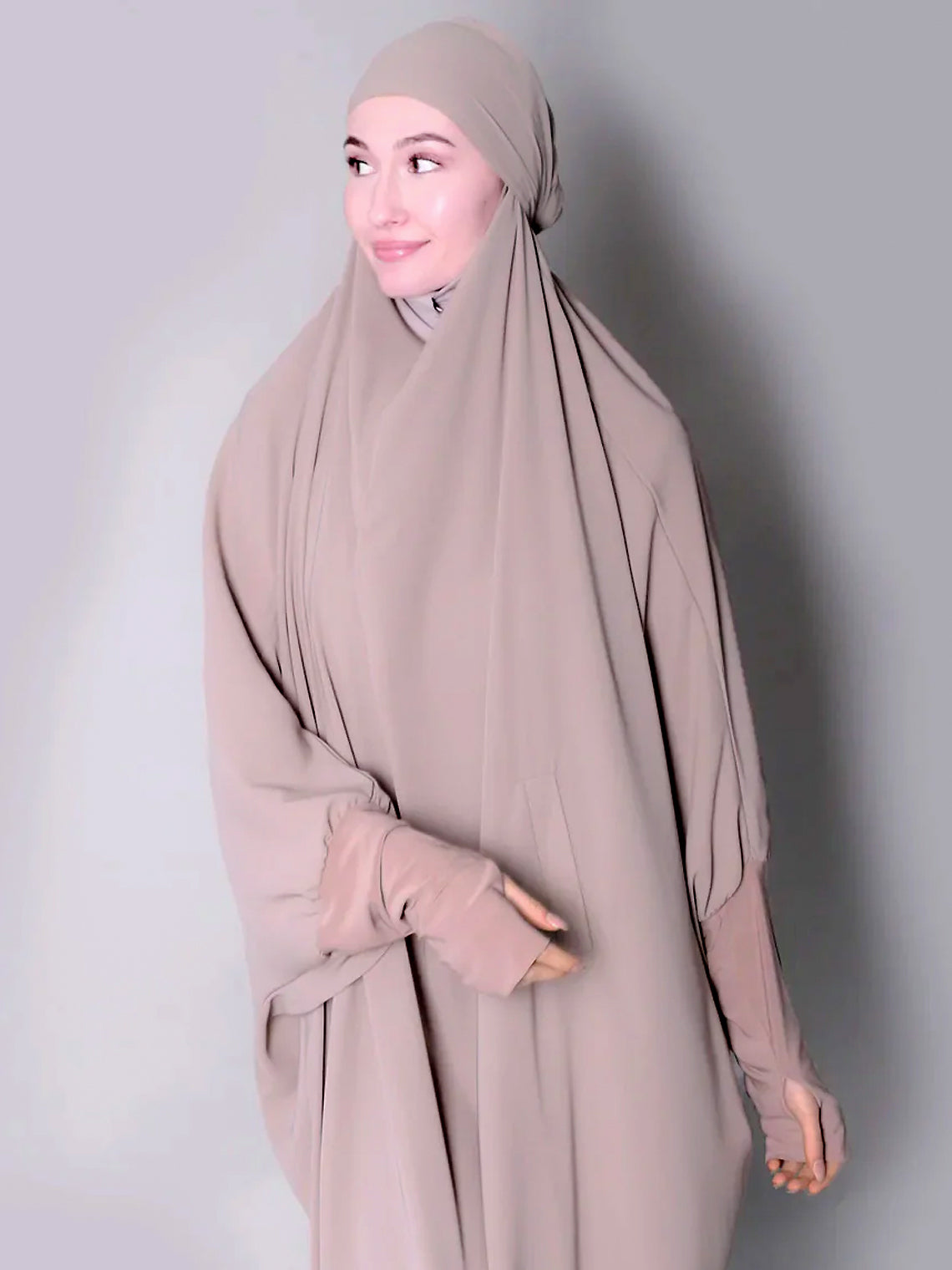 Woman wearing a beige hijab and dress against a plain background. one piece jilbab abaya