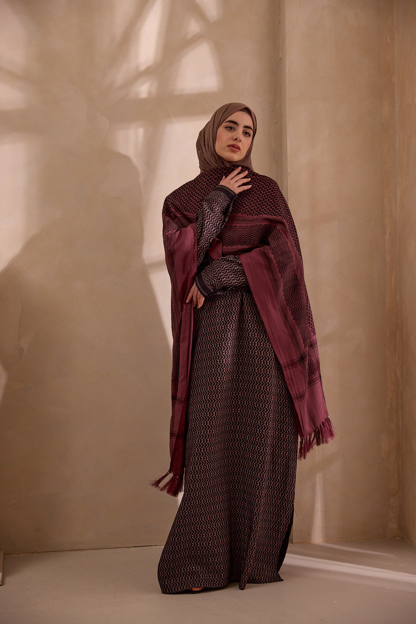 Woman wearing a patterned outfit with a maroon scarf against a beige wall.