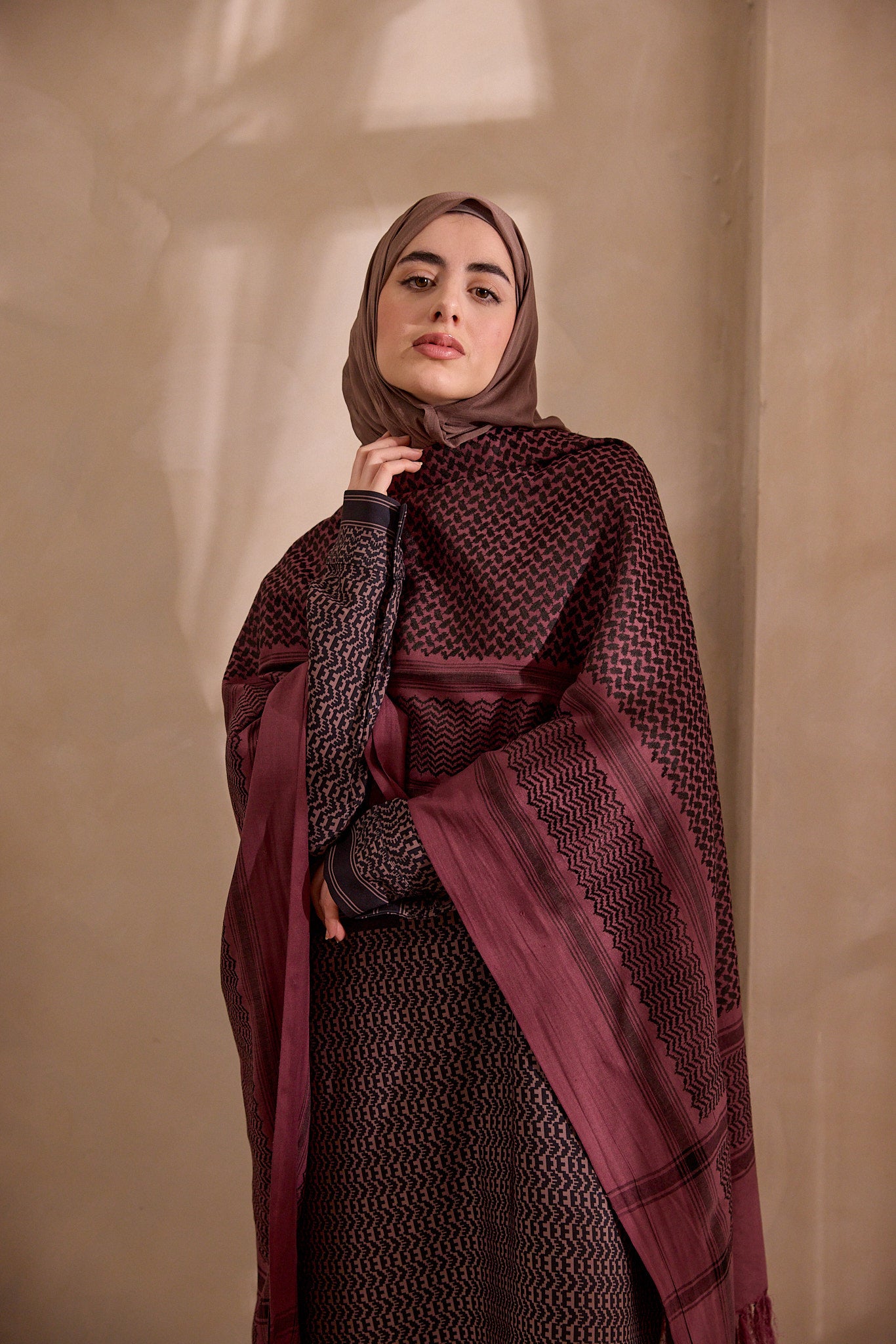 Woman wearing a patterned burgundy hijab against a beige background